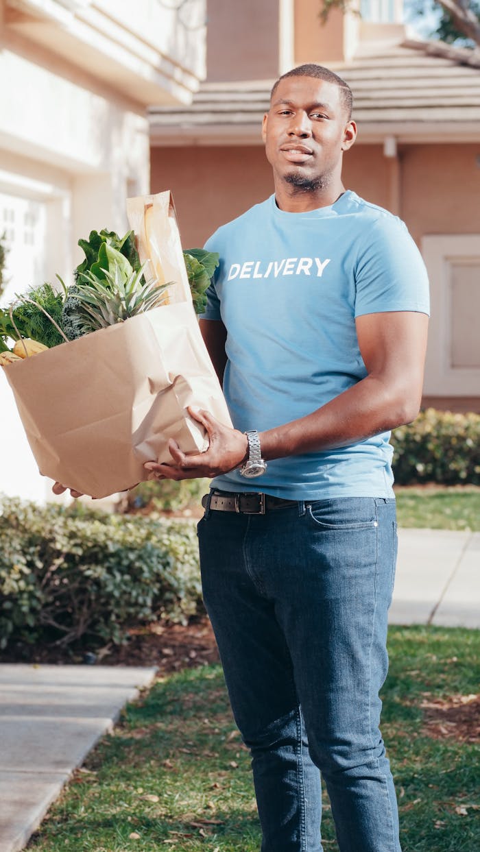 story-01 Smiling delivery man holding a paper bag of groceries on a sunny day outdoors.